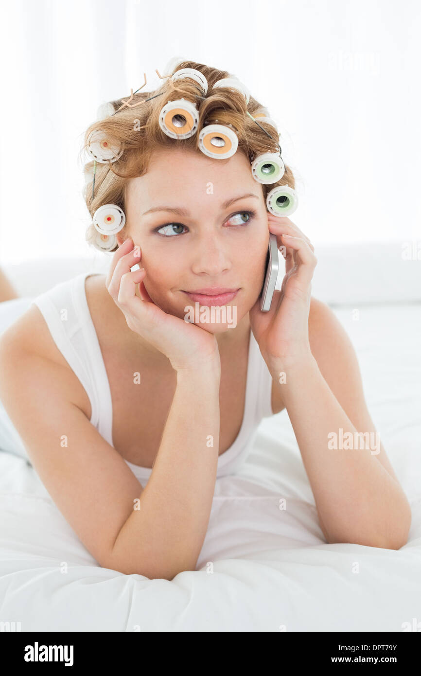 Femme dans les bigoudis using cellphone while Lying in Bed Banque D'Images