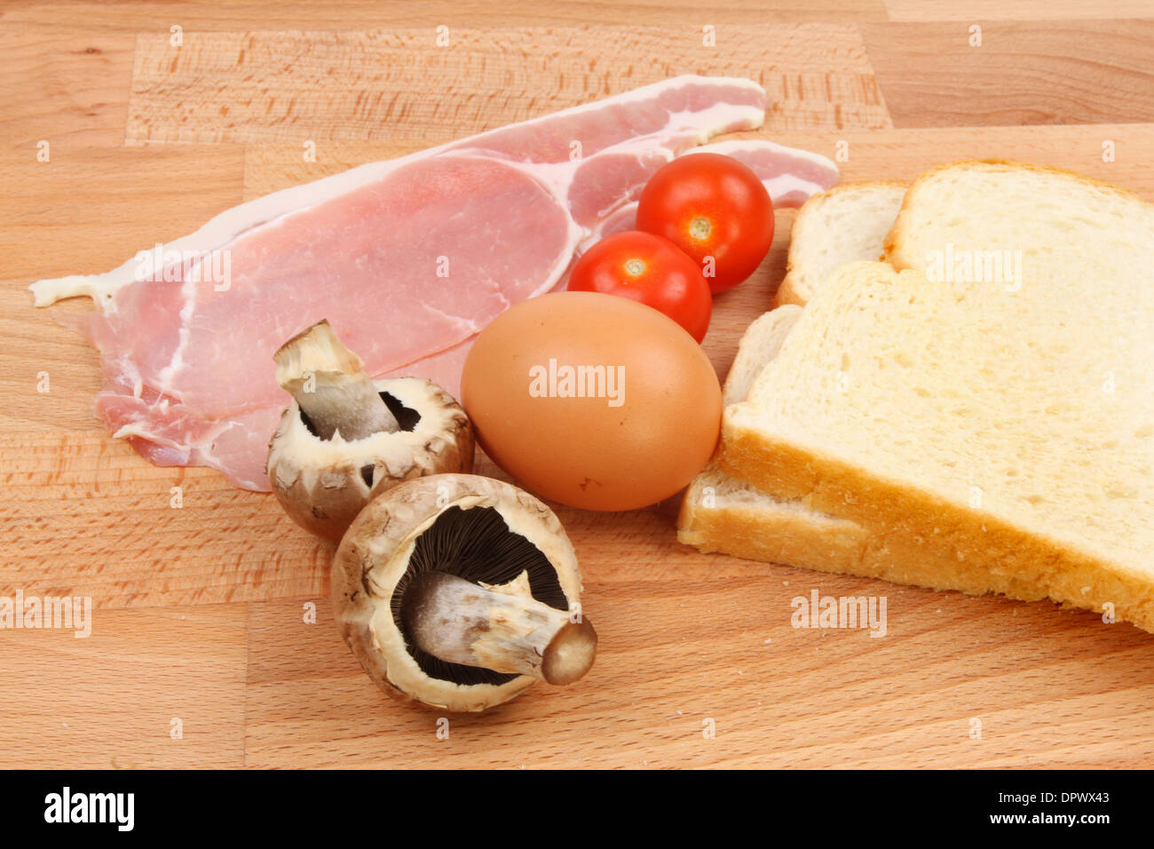 Ingrédients pour le petit-déjeuner, bacon, oeufs, tomates, champignons et de pain sur un plan de travail en bois Banque D'Images