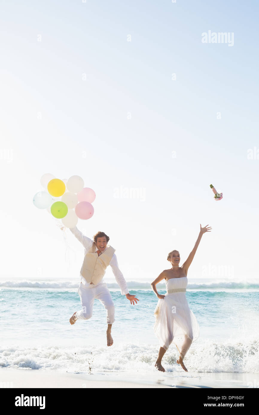 Groom holding balloons et épouse de jeter son bouquet sautant Banque D'Images