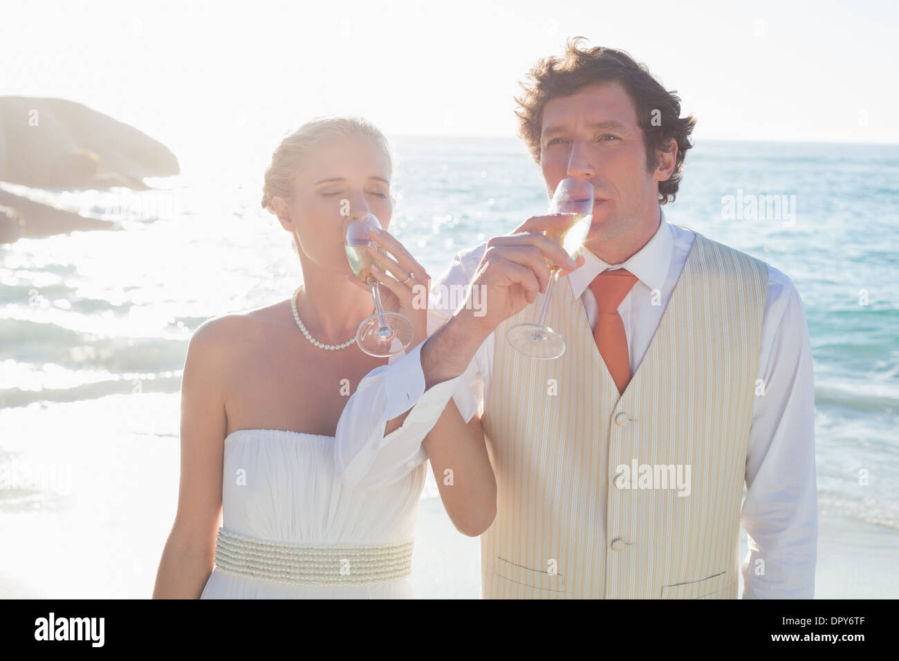 Les jeunes mariés drinking champagne linking arms Banque D'Images