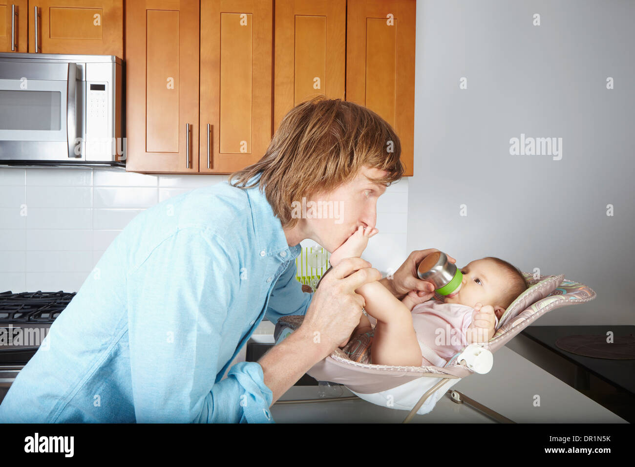 Father kissing baby's feet in chair Banque D'Images