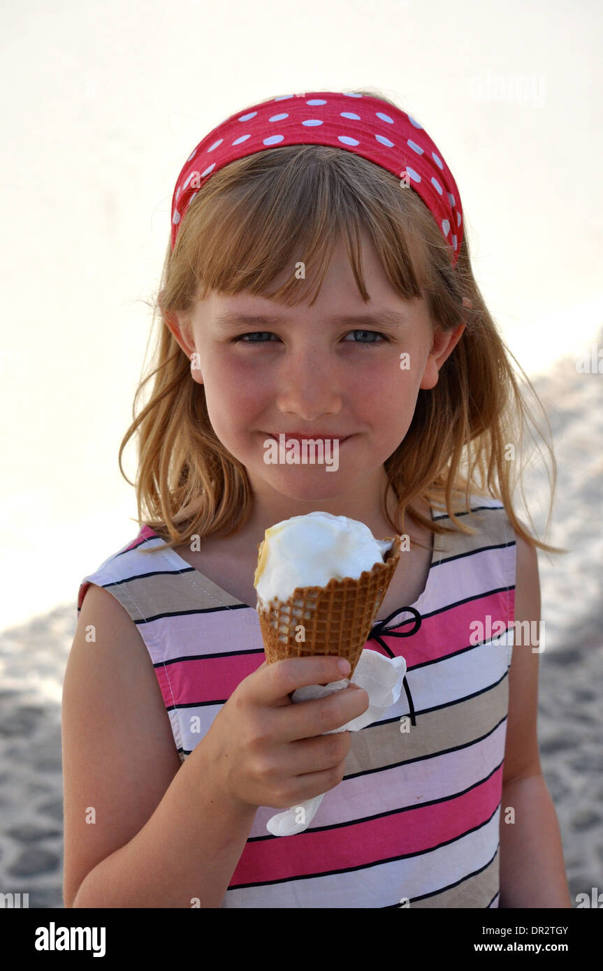 Le portrait de la petite fille blonde manger une glace à la vanille en vacances dans un blanc à rayures et robe rose à pois et d'un sèche-bande Banque D'Images