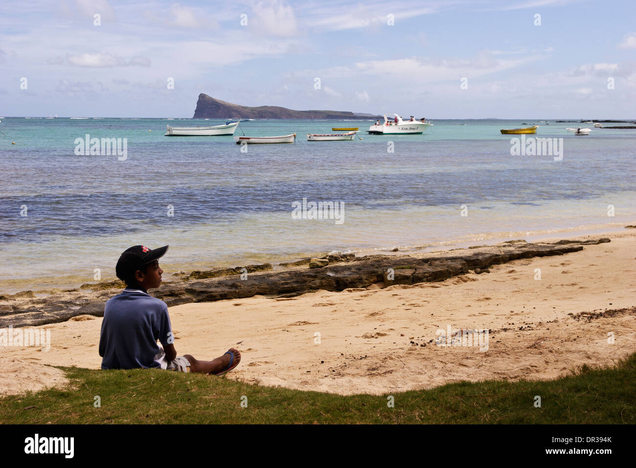 Garçon assis sur la plage et l'île de coin de mire dans la distance, l ...