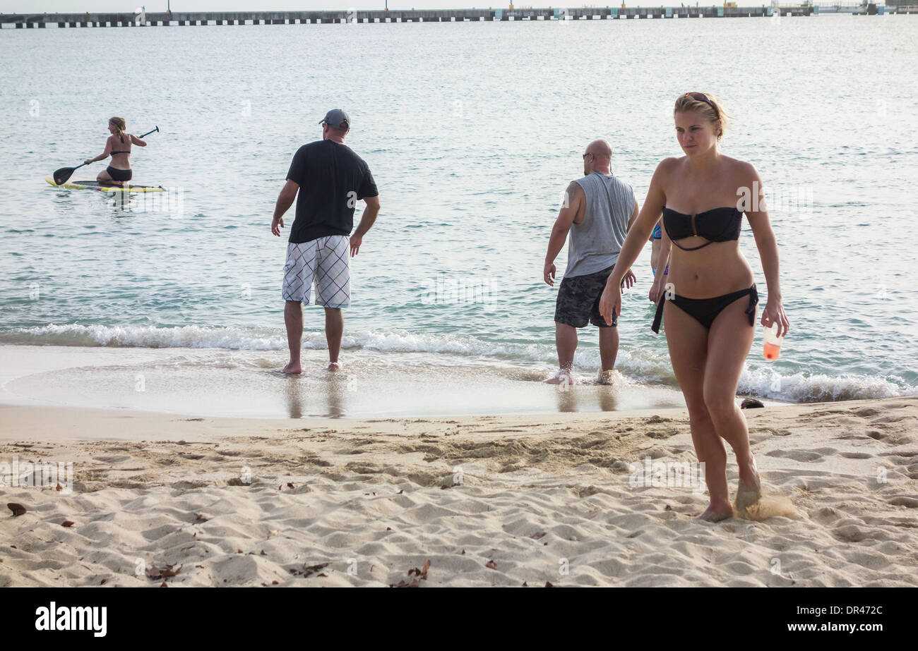 Deux hommes regarder avec intérêt en tant que femme paddles un conseil sur les Caraïbes, tandis qu'une autre femme entre à l'intérieur des terres. Portrait.St. Croix,U.S. Îles Vierges britanniques. Banque D'Images