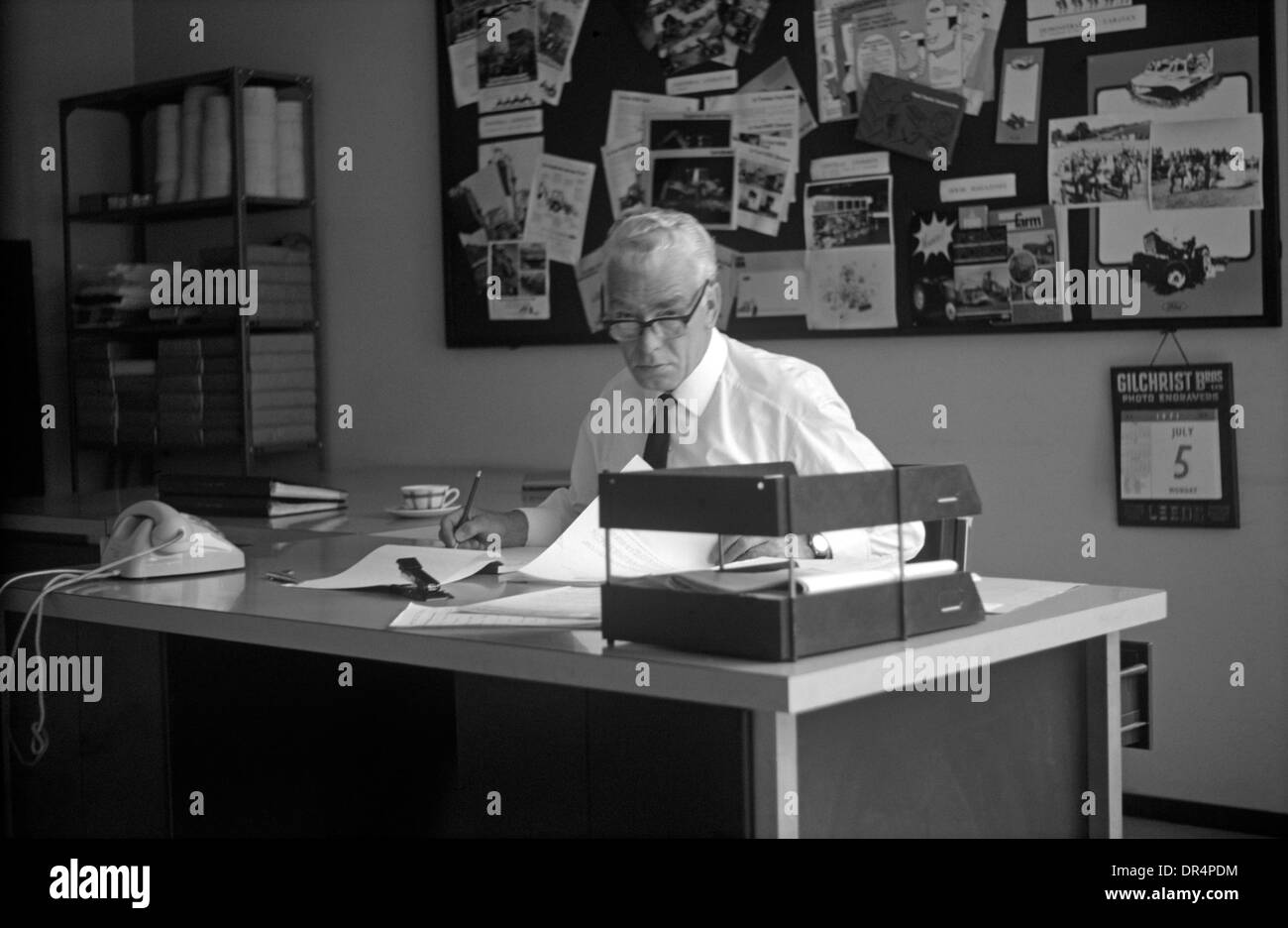 Un homme d'âge moyen regarde à partir de la paperasse pendant une journée  de travail à son bureau de Bruxelles 1970 Photo Stock - Alamy