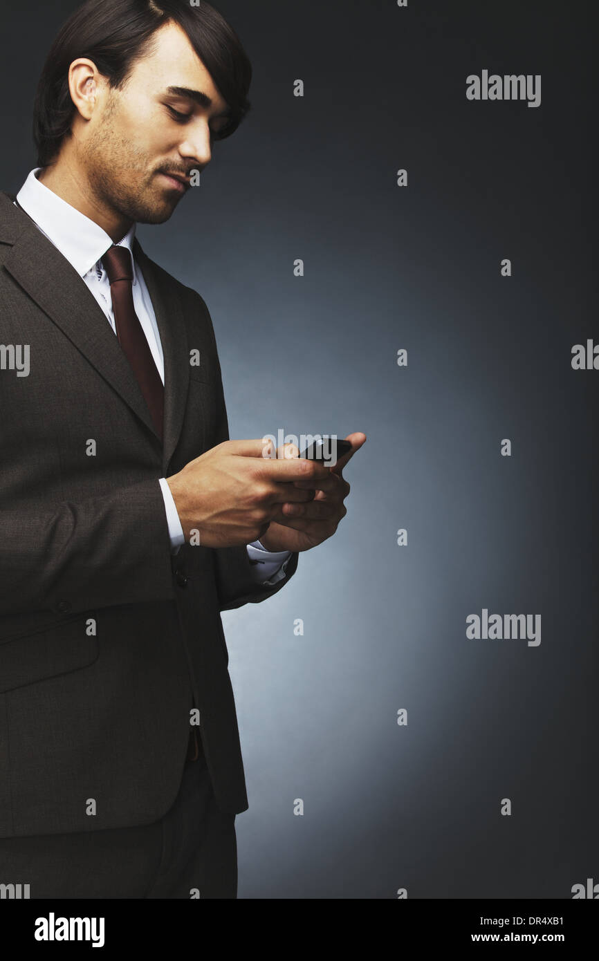 Portrait of young businessman using mobile phone messagerie texte sur fond noir. Modèle masculin asiatique en utilisant un téléphone cellulaire. Banque D'Images