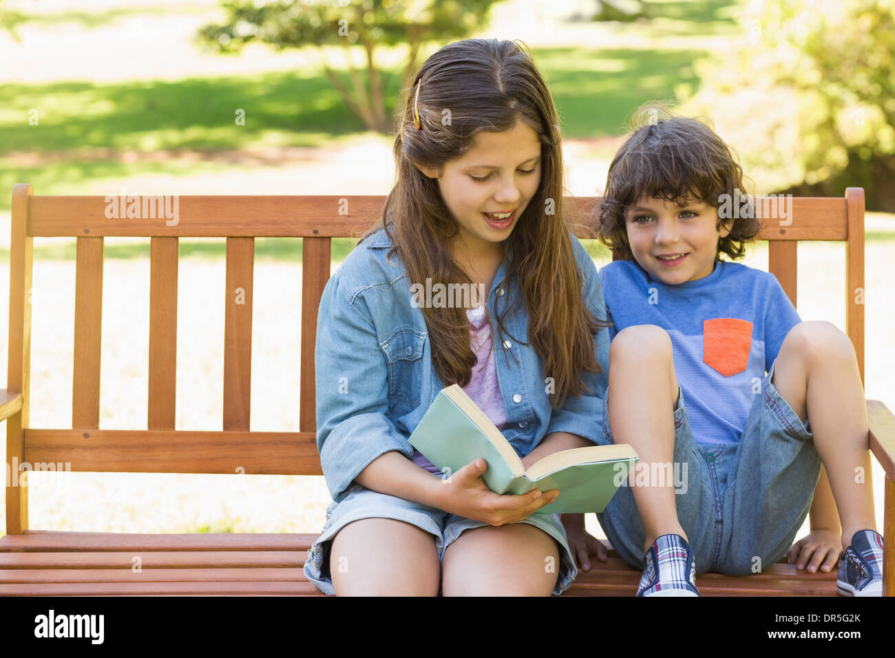 Kids reading book on park bench Banque D'Images