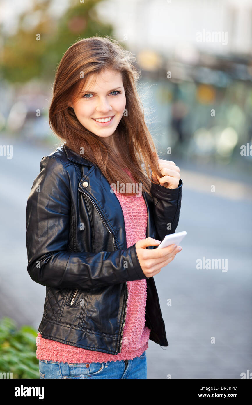 Belle adolescente en utilisant son téléphone intelligent dans la ville Banque D'Images