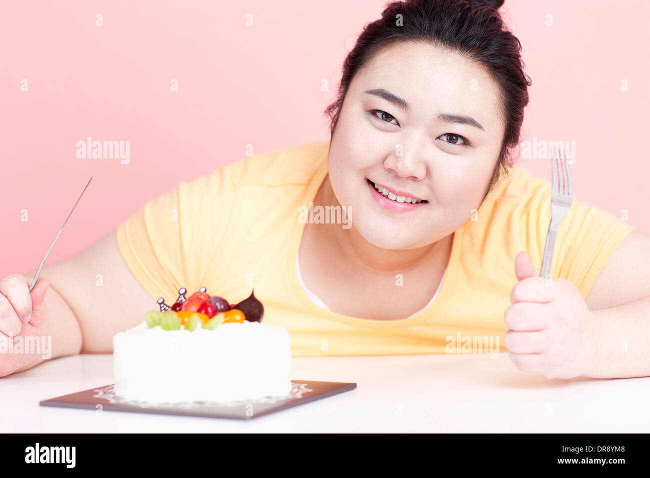 Une femme grassouillette avec un gâteau devant elle Banque D'Images