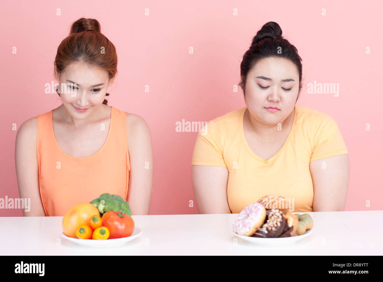 Une fine et grassouillet femme assise à table avec des aliments différents à l'avant Banque D'Images