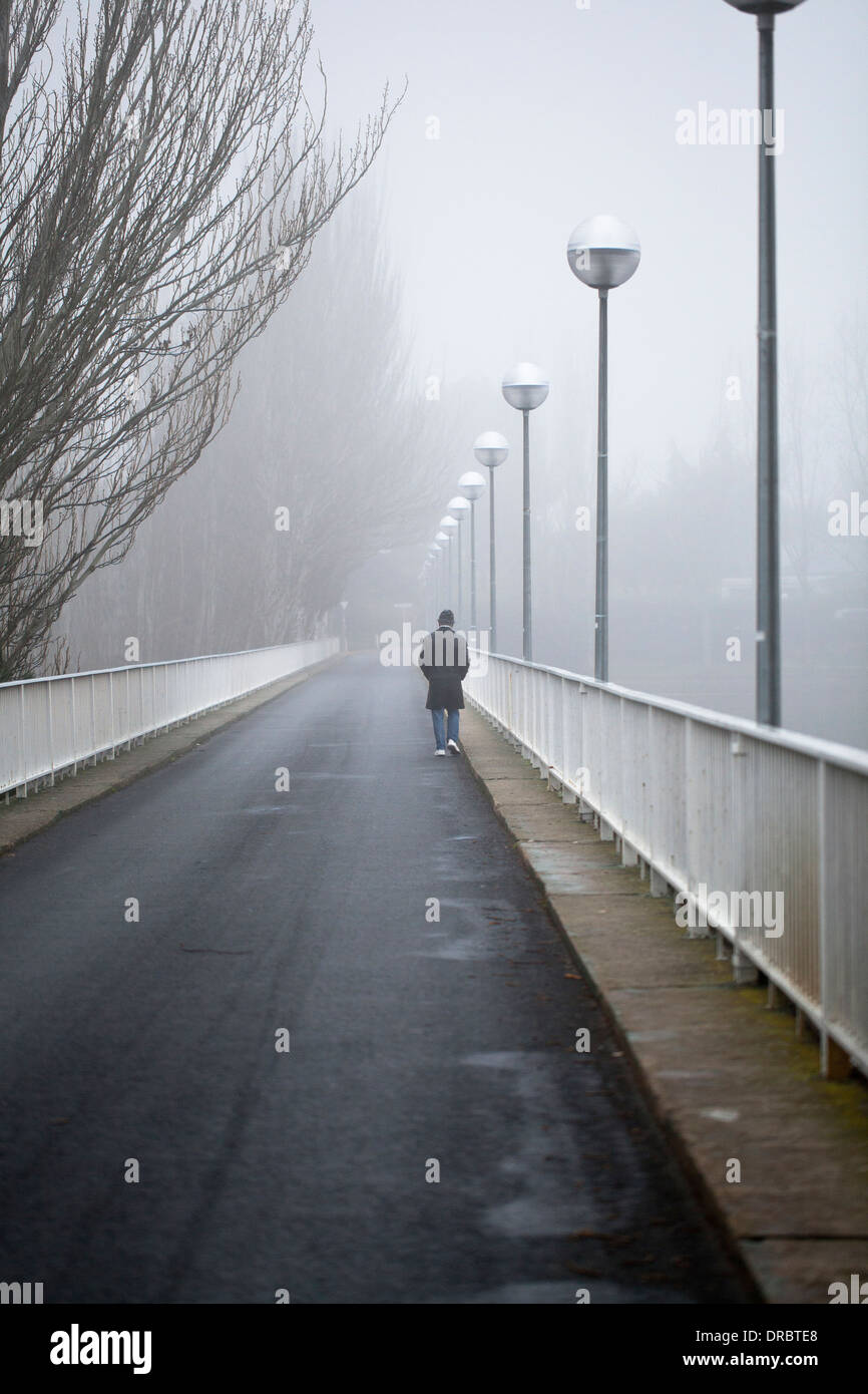 Un homme traverse un pont au-dessus d'un lac un jour brumeux Banque D'Images