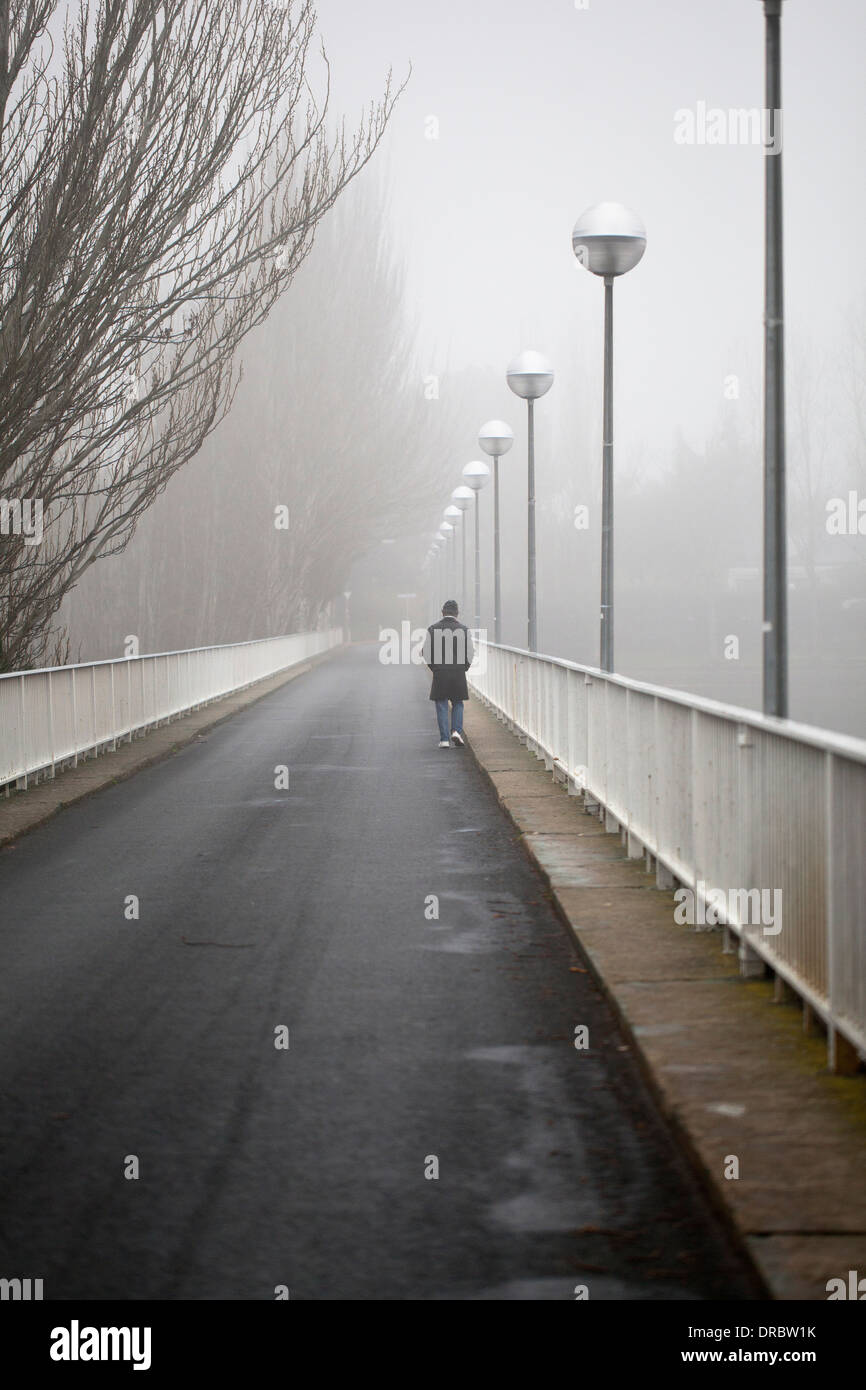 Un homme traverse un pont au-dessus d'un lac un jour brumeux Banque D'Images