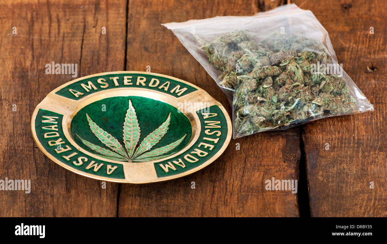 Cendrier avec signe d'Amsterdam et un grand sac de plastique de la lutte contre les mauvaises herbes ou de la marijuana sur fond de bois Banque D'Images