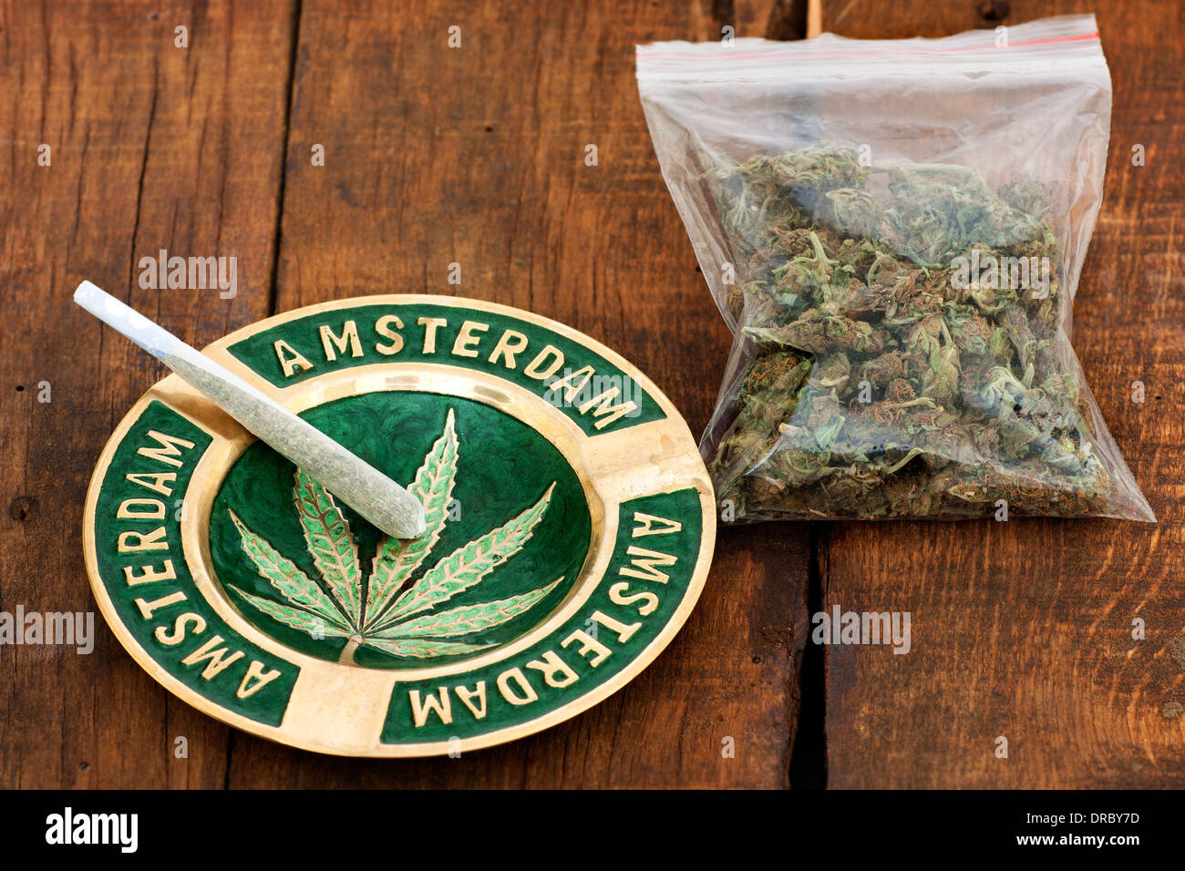 Joint de marijuana dans un cendrier avec signe d'Amsterdam et un grand sac de plastique de la lutte contre les mauvaises herbes sur fond de bois Banque D'Images
