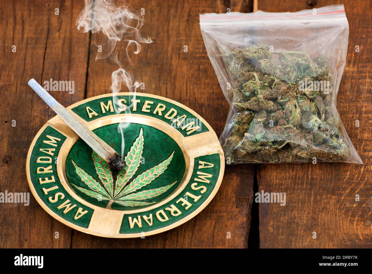 Fumer du cannabis Joint dans un cendrier avec signe d'Amsterdam et un grand sac de plastique de la lutte contre les mauvaises herbes sur fond de bois Banque D'Images