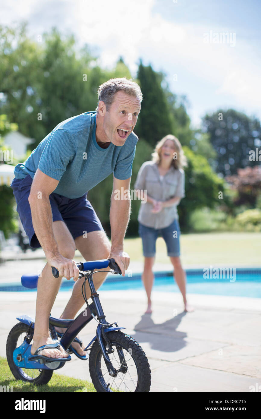 Petites Man riding bicycle at poolside Banque D'Images