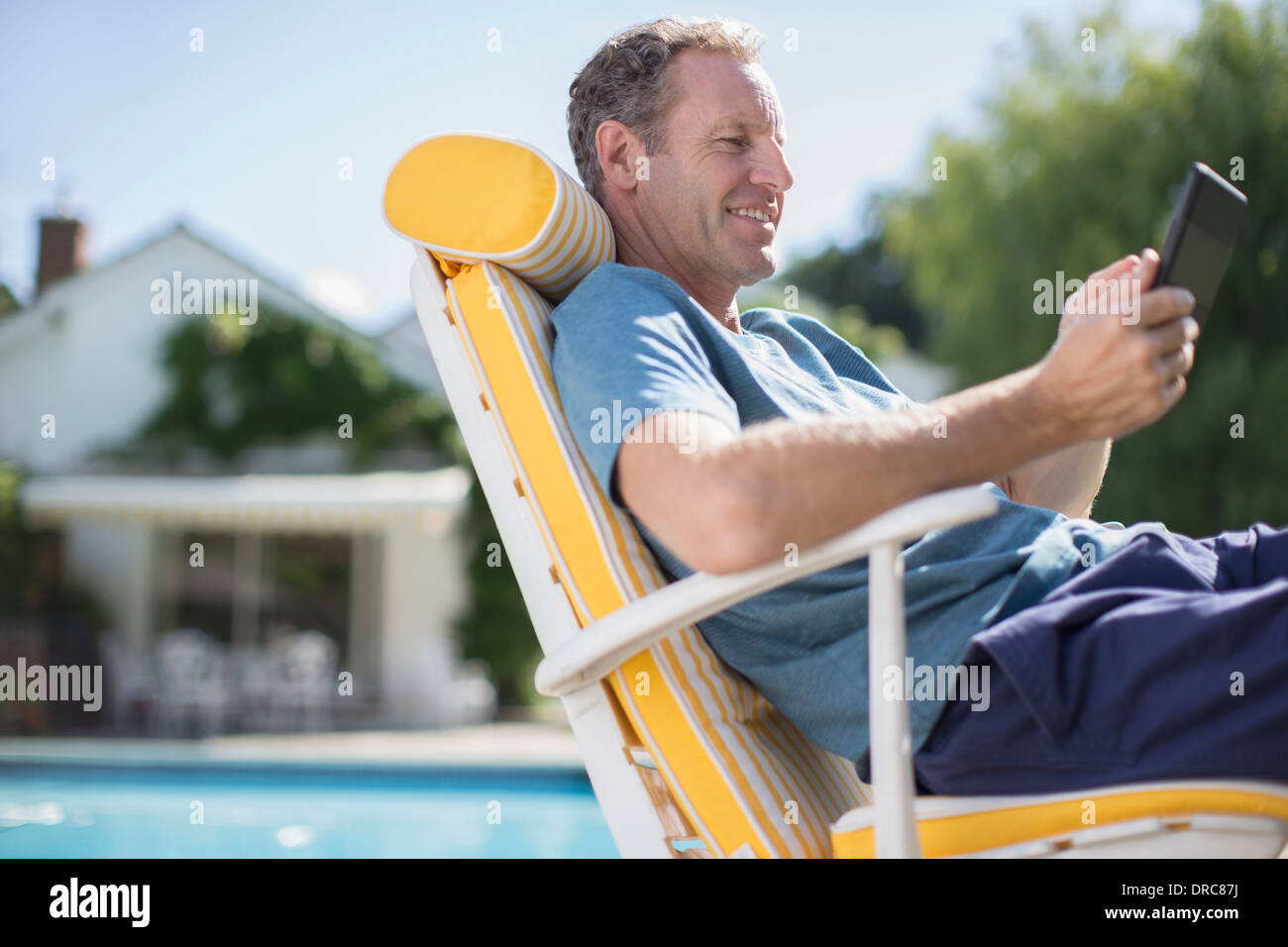 Man reading in lounge chair at poolside Banque D'Images