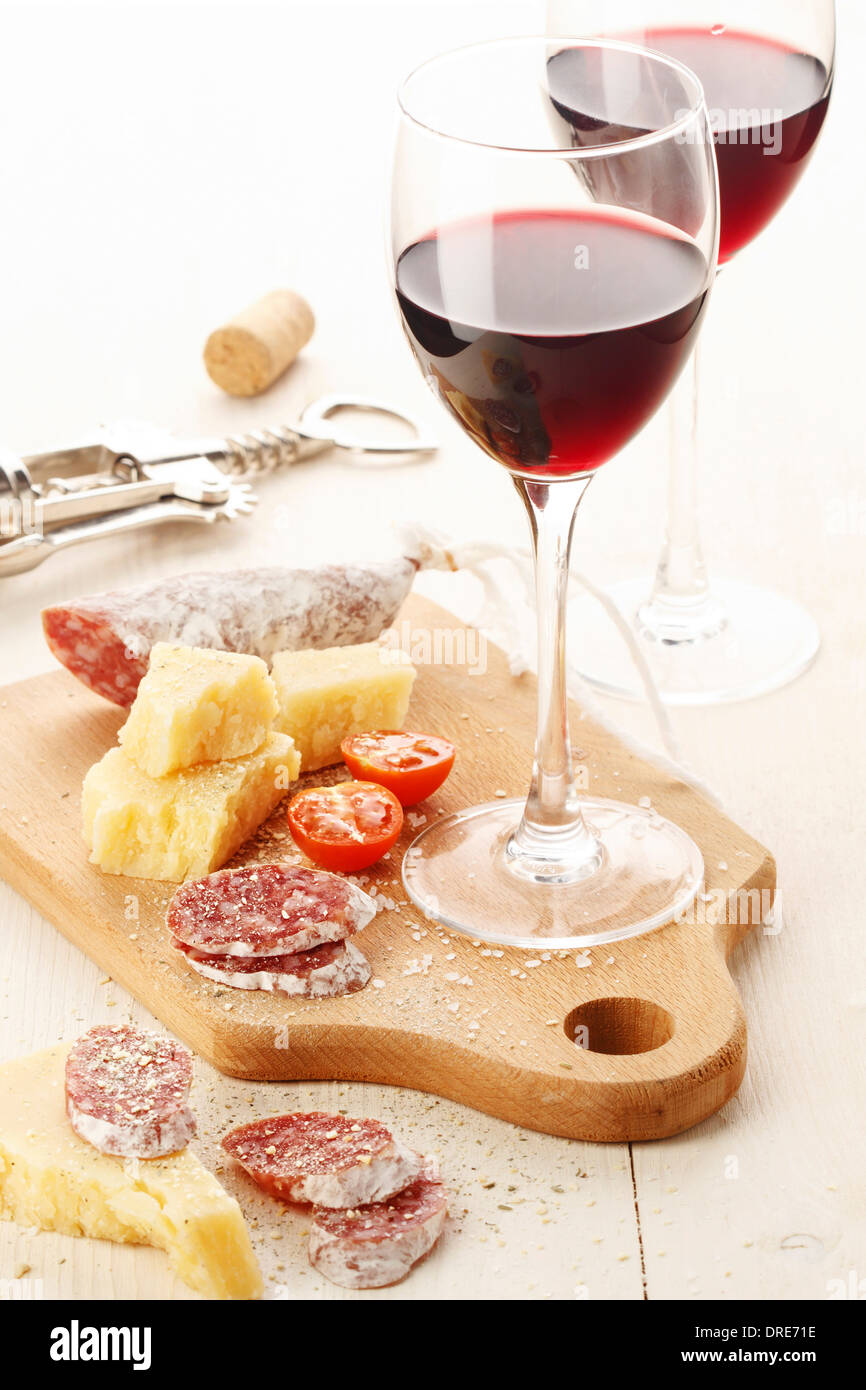 Deux wineglasses avec vin rouge et assortiment de fromages et fruits sur fond blanc Banque D'Images