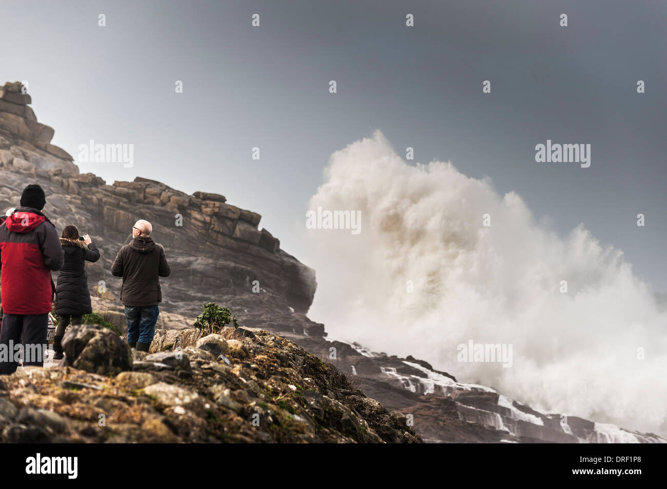 Les touristes regarder comme très grand les vagues déferlent sur des rochers à Sennen Cove, à Cornwall. Banque D'Images
