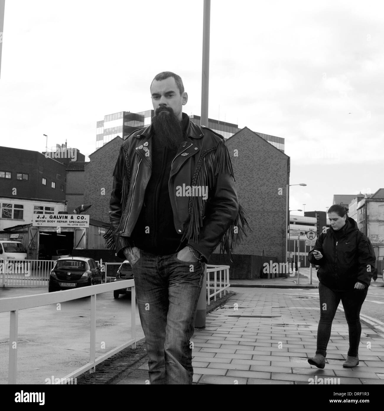 Grand homme blanc avec longue barbe et noir veste biker en marchant avec les mains dans les poches à Luton Banque D'Images