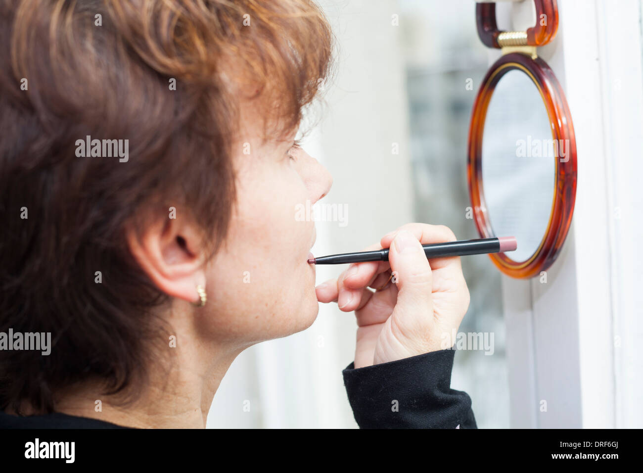 Femme d'âge moyen et à l'application d'un crayon à lèvres dans le miroir. Banque D'Images