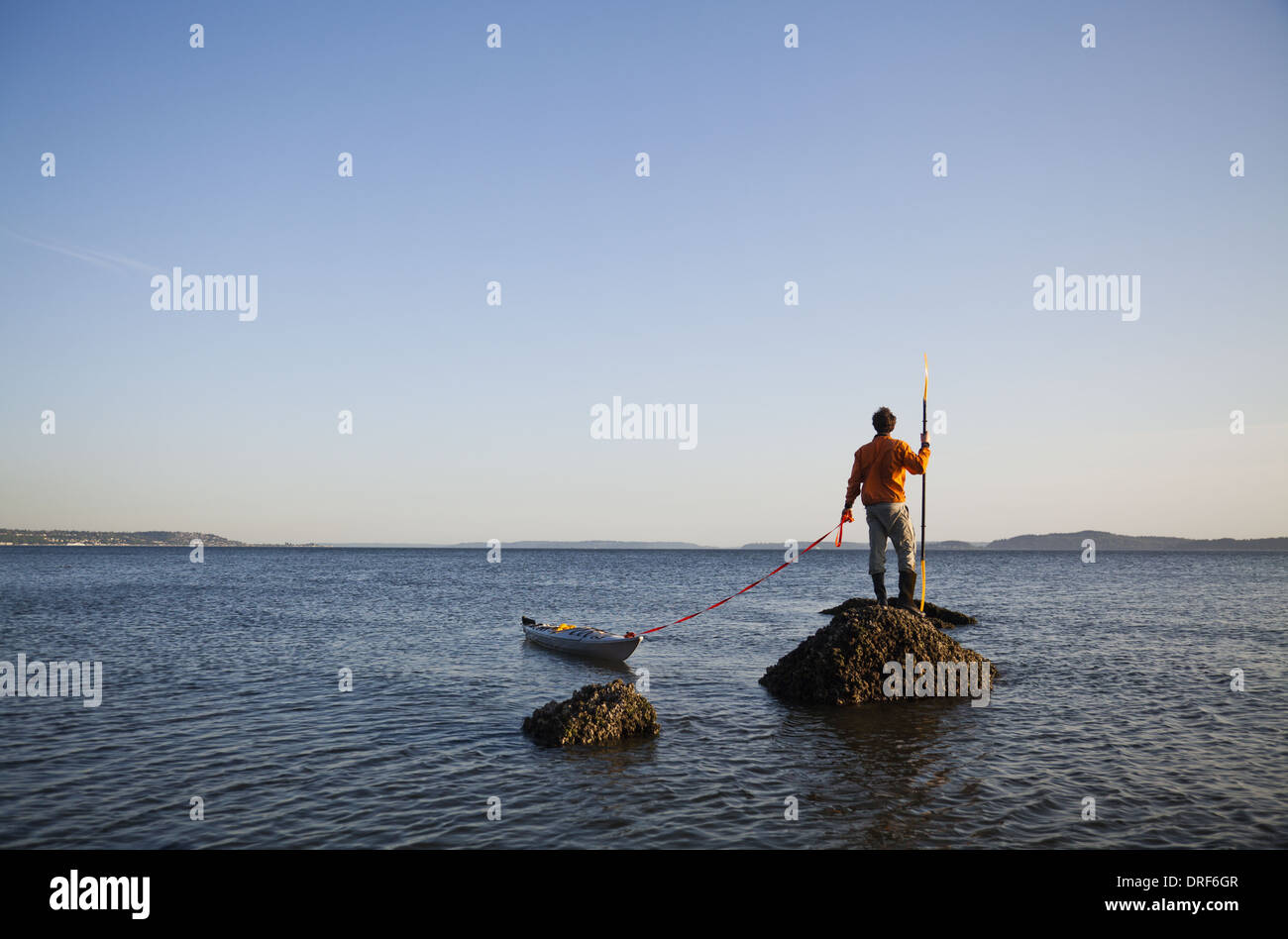 Seattle Washington USA kayakiste de mer se dresse sur roche dans la mer au coucher du soleil Banque D'Images