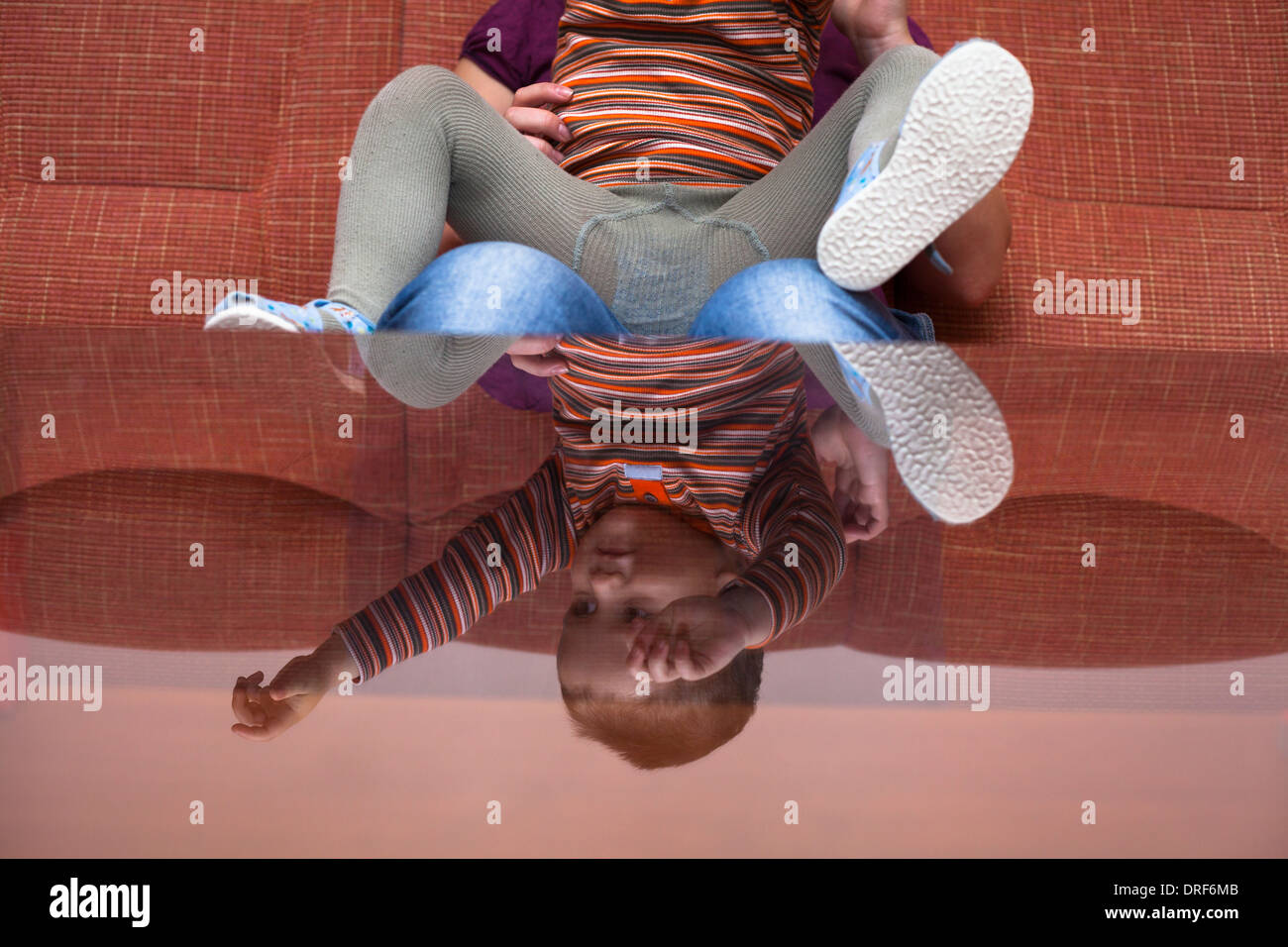 Garçon enfant ludique reflète dans une table en verre sitting on sofa at home Banque D'Images