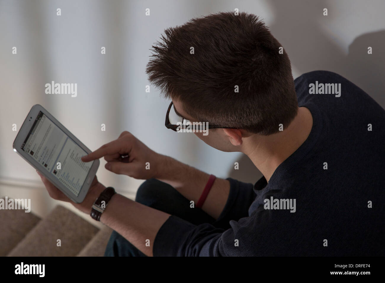 Plus de coup d'épaule de l'homme portant des lunettes de l'affichage d'un site web de réseautage sur l'écran tactile tablette numérique. Banque D'Images