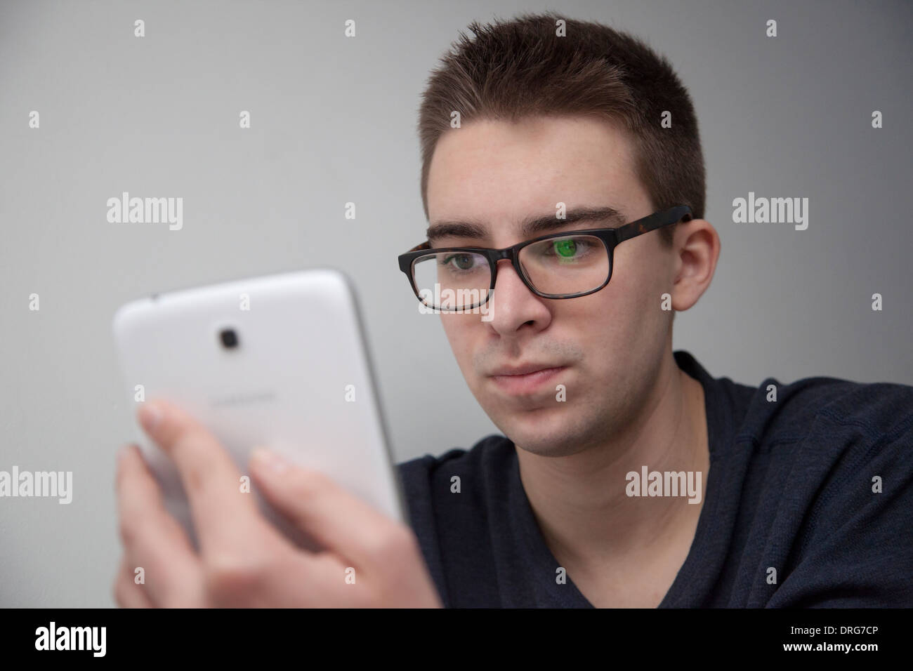 Jeune homme portant des lunettes assis à l'aide d'une mini tablette numérique. Vue de face. Banque D'Images