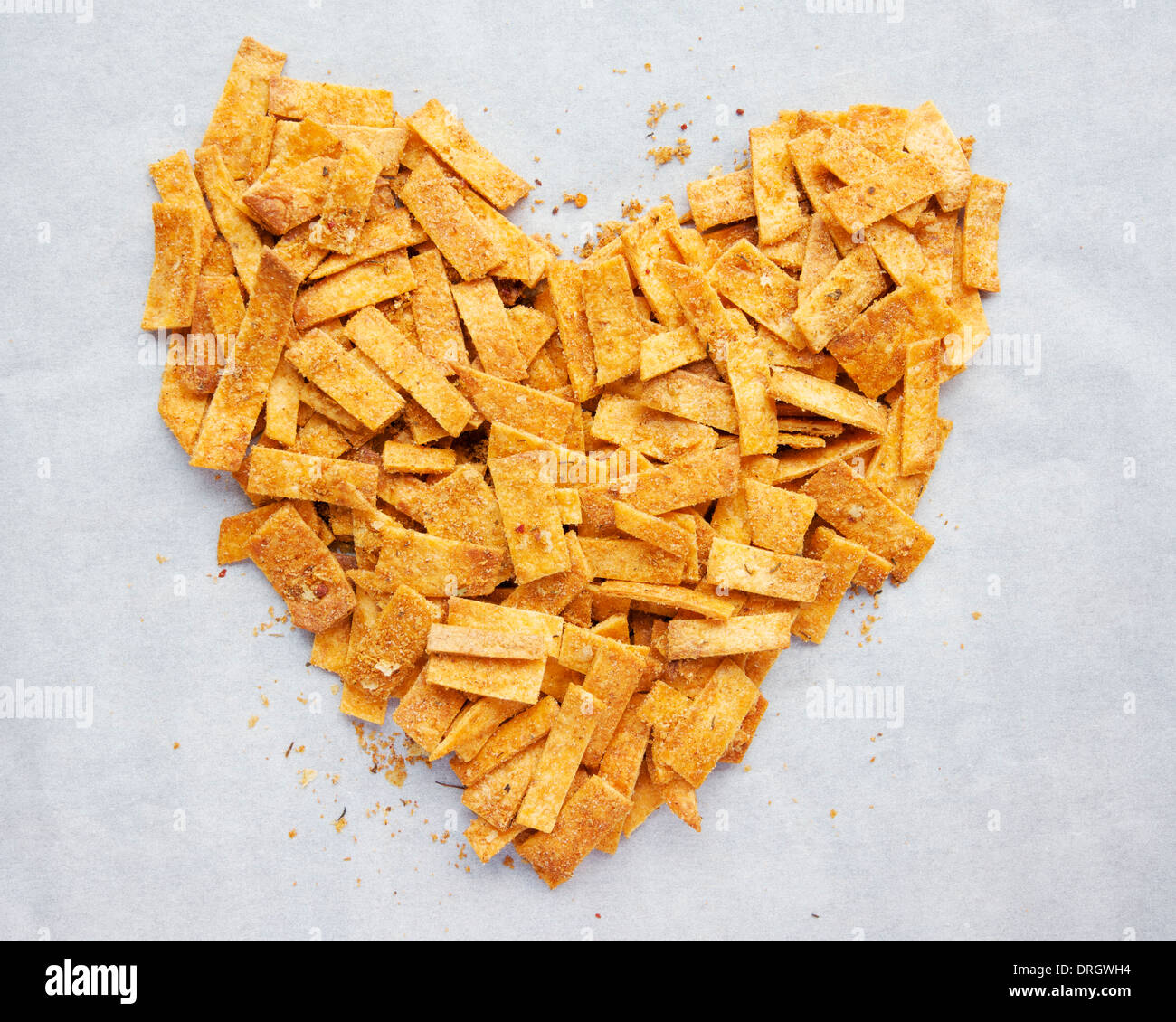 Des bandes de chips tortilla de farine épicée, disposées en forme de coeur sur le papier parchemin. Banque D'Images