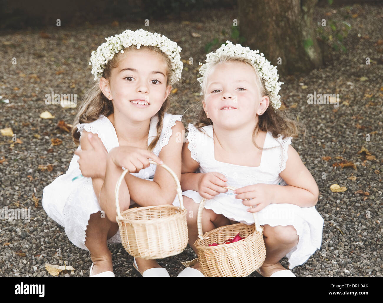 Deux petites filles habillés pour un mariage. Les filles sont s'inclina en souriant et en regardant la caméra. Banque D'Images