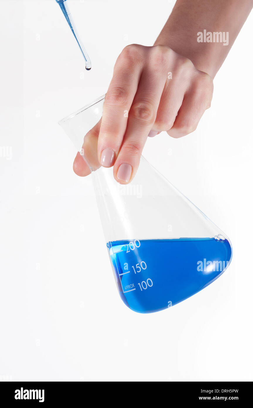Un scientifique l'ajout de gouttes d'une solution d'une pipette dans une fiole conique avec une solution de bleu Banque D'Images