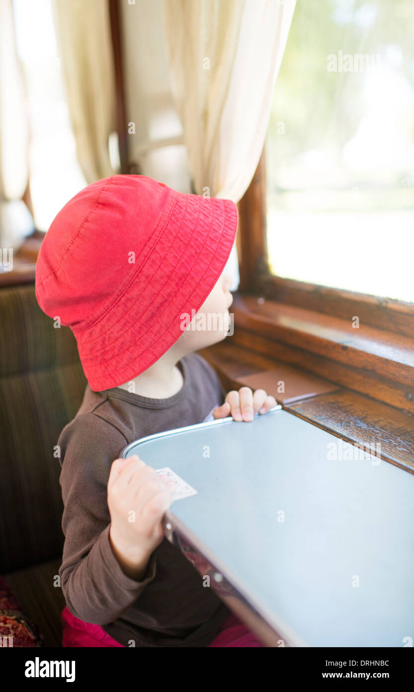 Petite fille avec red hat en regardant par la fenêtre dans un vieux train de passagers Banque D'Images