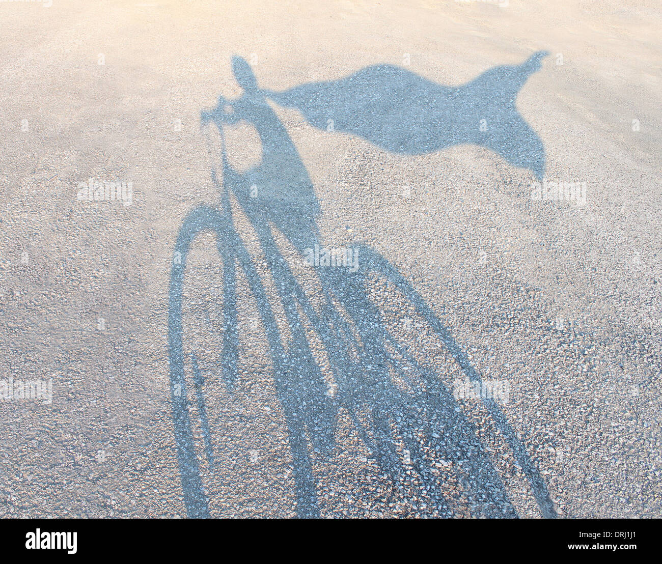 Super héros enfant portant une cape d'une bicyclette comme une ombre en fonte sur une route se faisant passer pour un héros puissant comme une métaphore et symbole de la jeunesse et l'enfance de l'imagination et l'autonomisation des enfants l'estime de soi. Banque D'Images