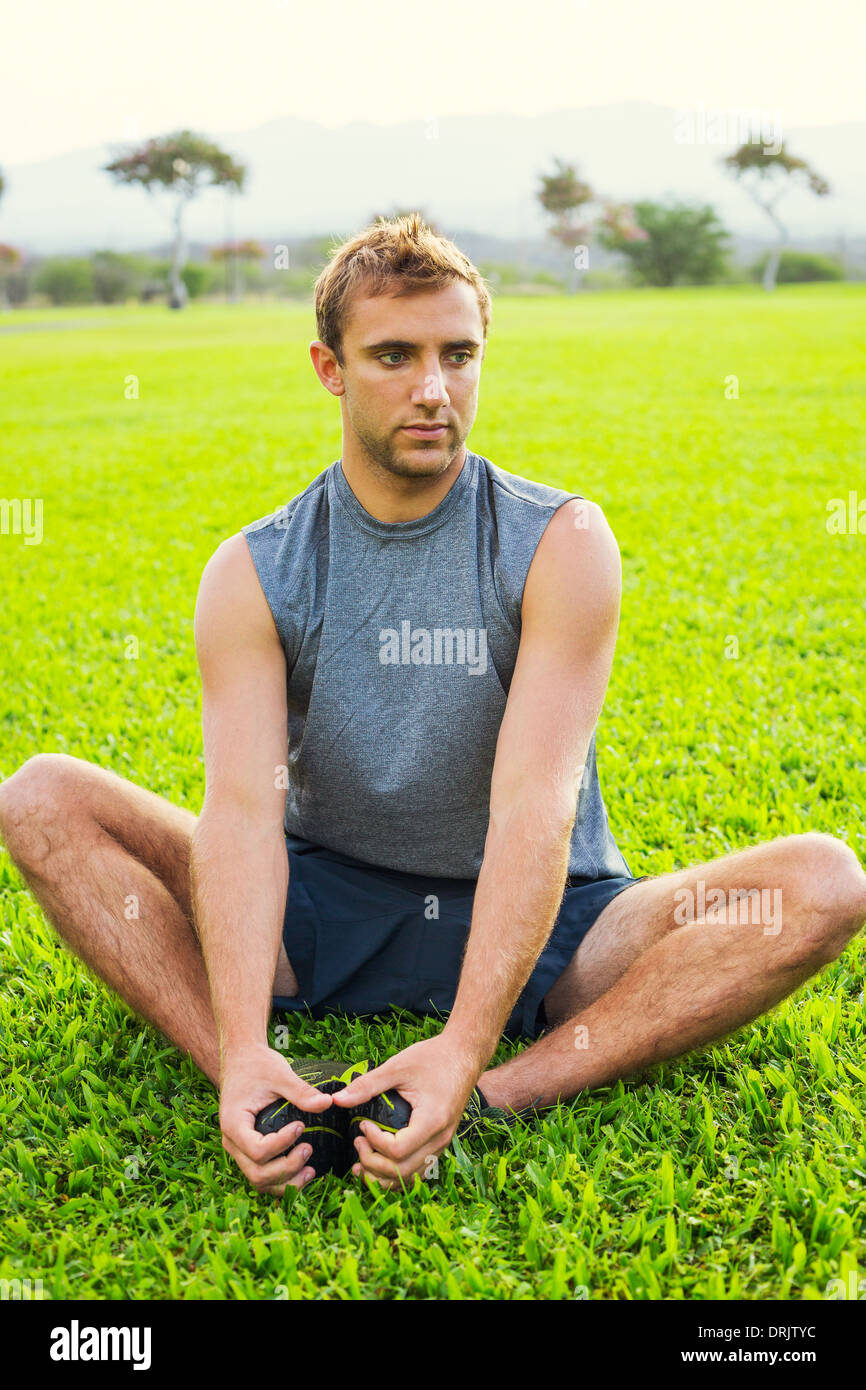 Jeune homme fit attrayants les étirements avant l'exercice, le lever du soleil tôt le matin et rétroéclairées. Vie saine remise en forme sport concept. Banque D'Images