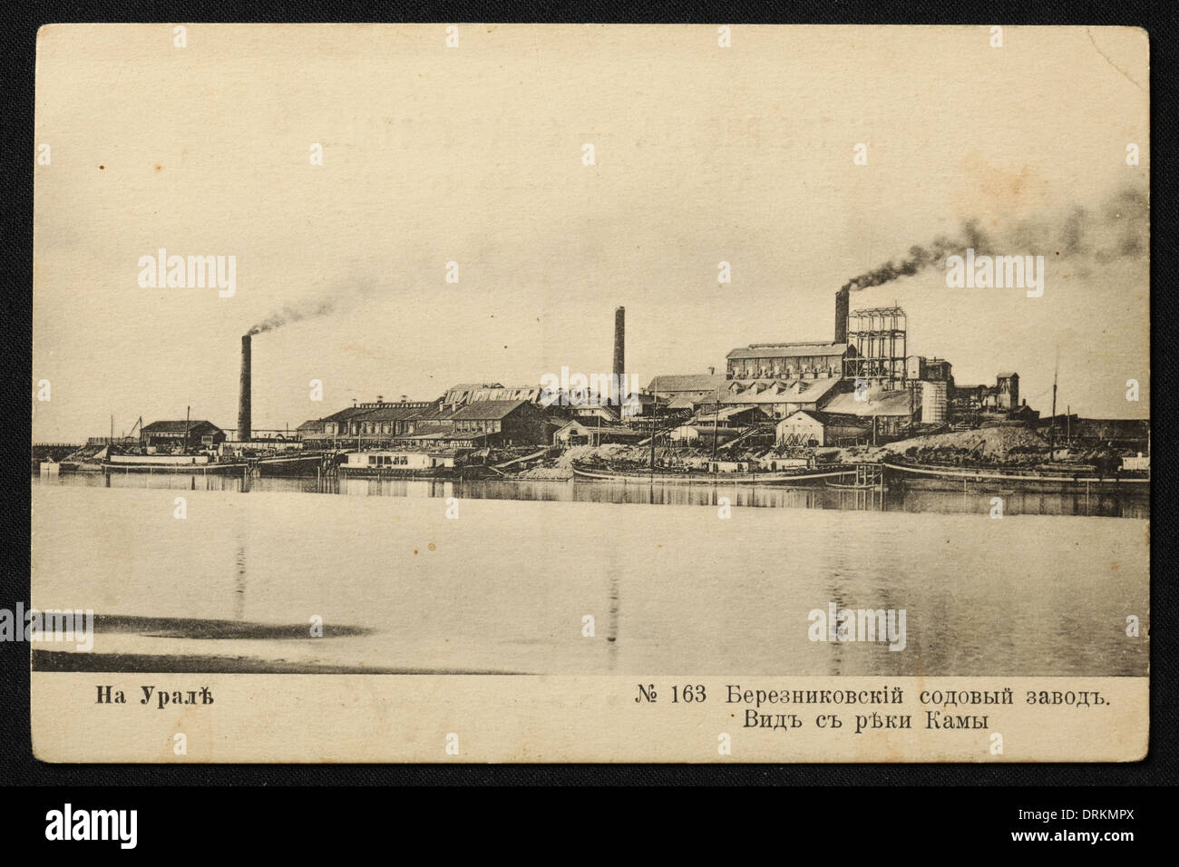 Usine de sodium et la rivière Kama à Berezniki dans les montagnes de l'Oural, Empire russe. Photo vintage noir et blanc du photographe russe Veniamin Metenkov datée du début du XXe siècle, publiée dans la carte postale russe vintage publiée par Veniamin Metenkov lui-même à Yekaterinburg, Russie. Texte en russe: Dans l'Oural. Usine de sodium Berezniki. Vue depuis la rivière Kama. Avec la permission de la collection de cartes postales Azoor. Banque D'Images