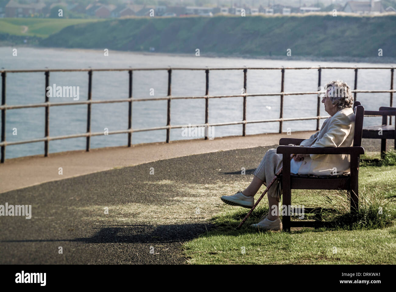 Femme caucasienne âgée assise sur un banc sur la promenade de Whitley Bay, Tyne et Wear Banque D'Images