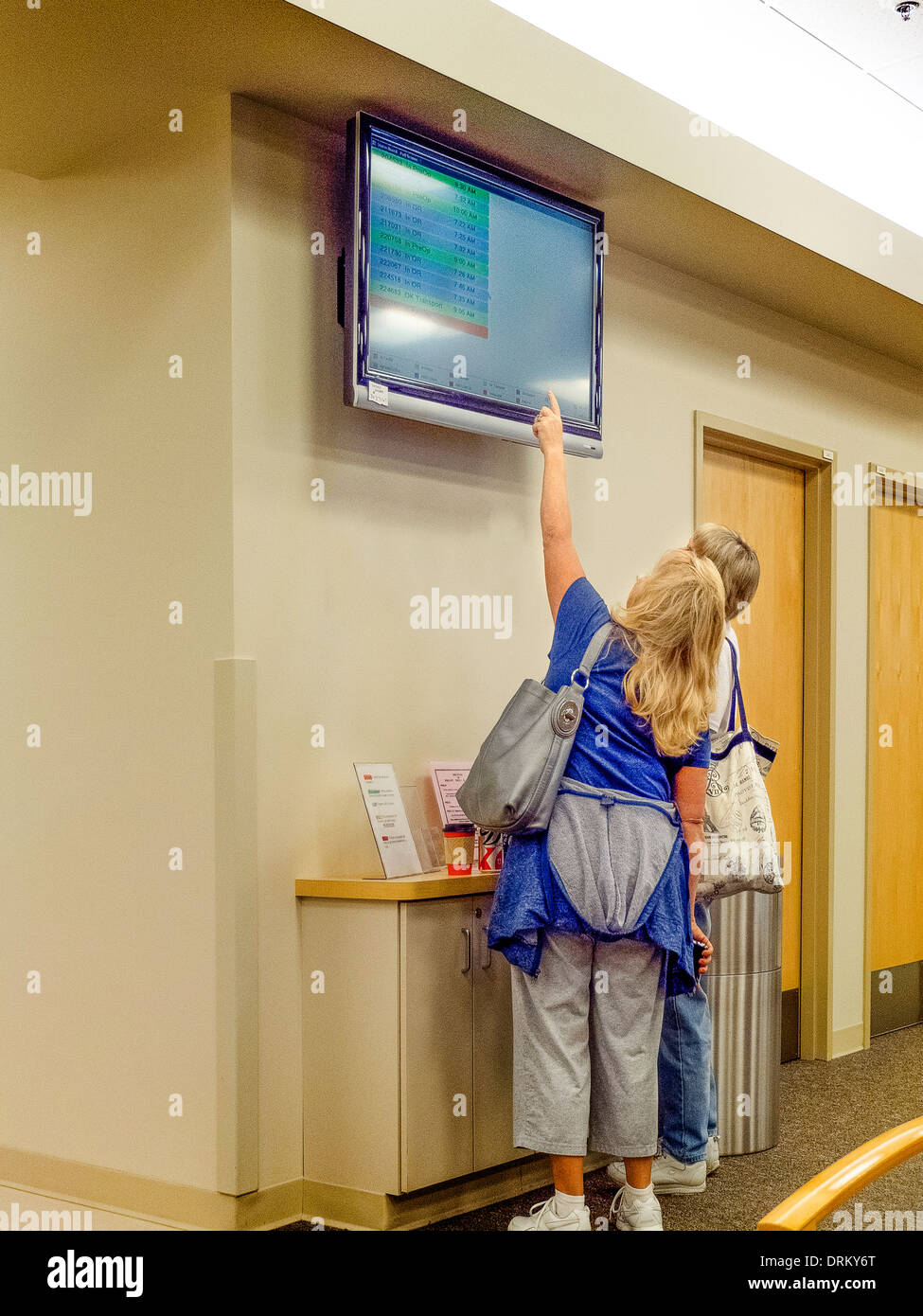 Parents d'un patient chirurgie de vérifier la progression de sa procédure sur un statut de la vidéo dans la salle d'attente d'un hôpital du Sud de la Californie. Banque D'Images