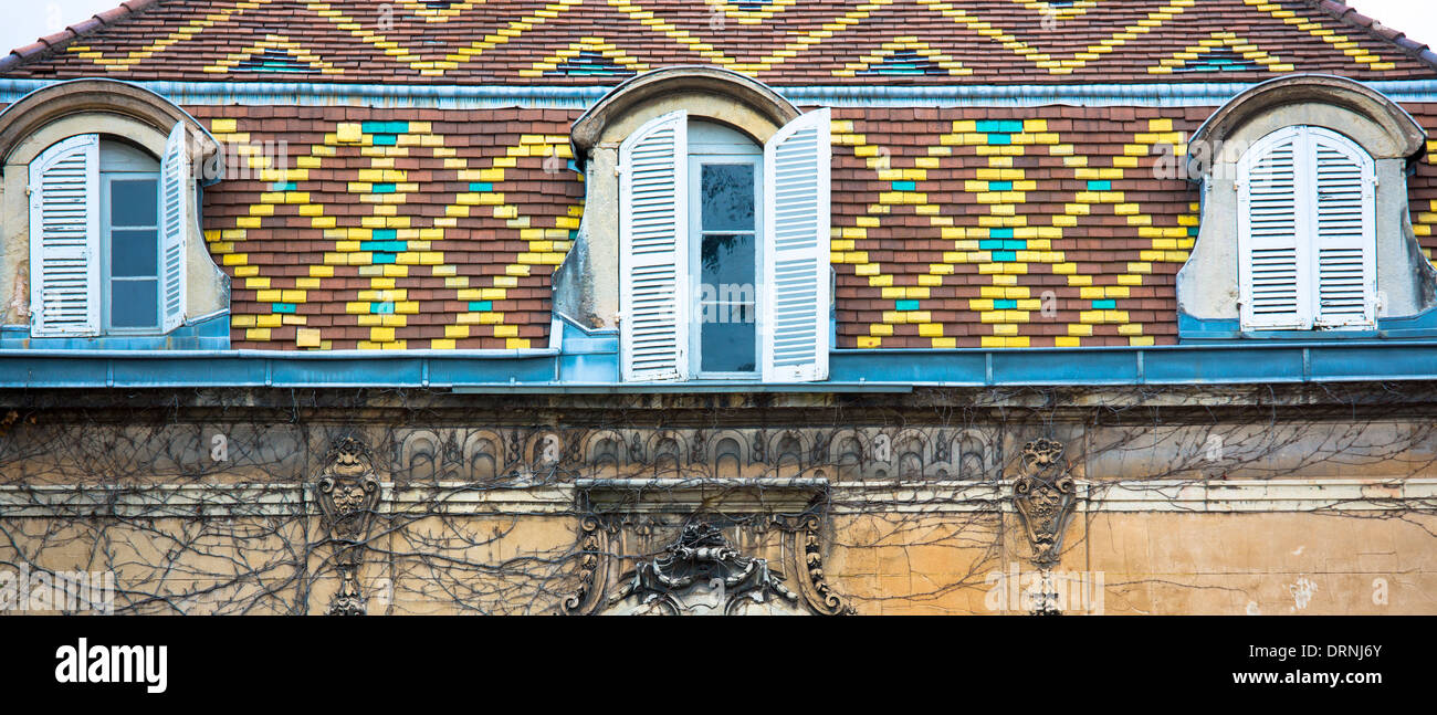 Toit de tuiles polychromes traditionnelles et de volets aux fenêtres sur un bâtiment d'époque à Dijon en Bourgogne, en France Banque D'Images