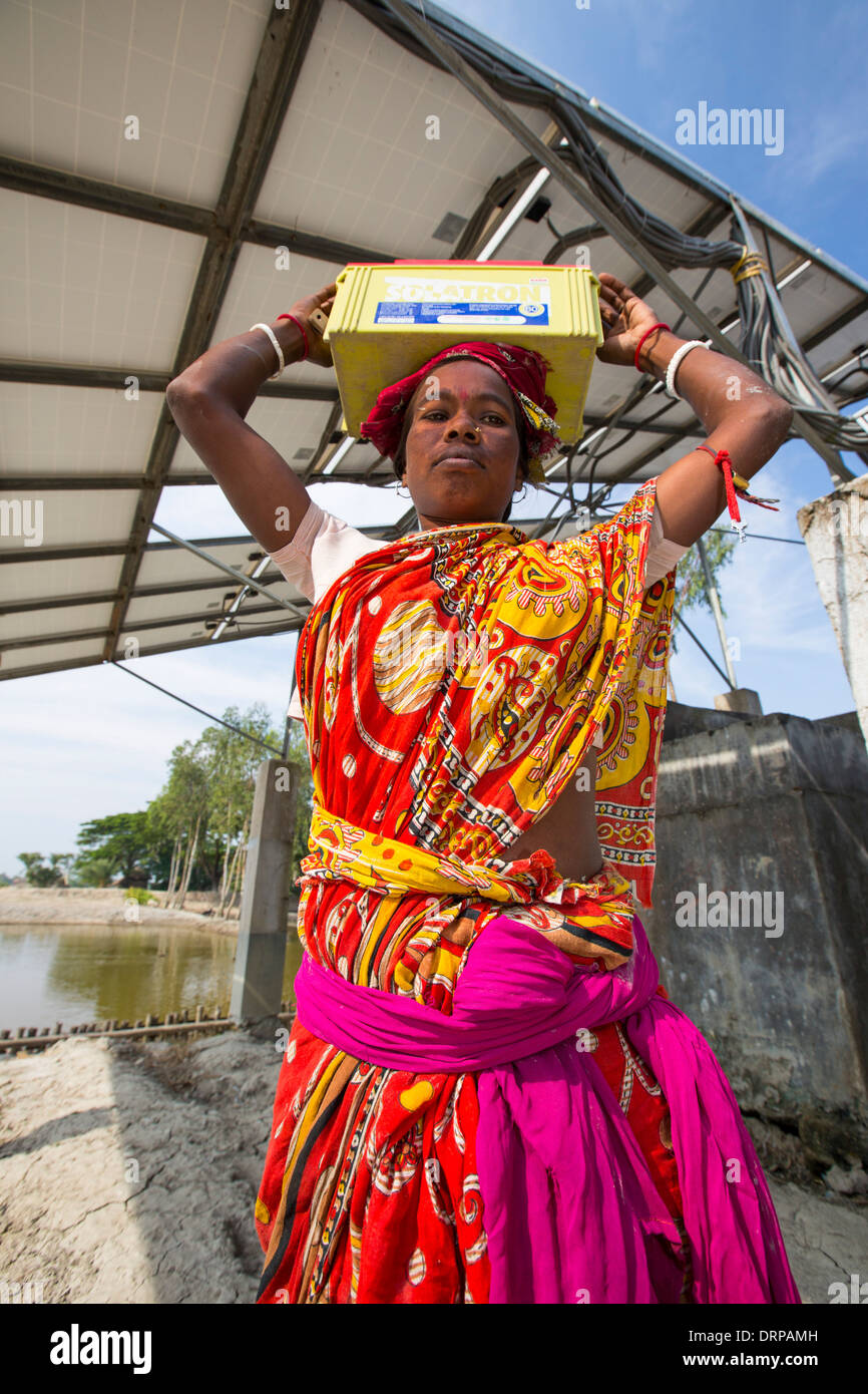 Un projet du WWF à fournir de l'électricité à une île isolée dans les Sunderbans, une zone de basse altitude du delta du Gange dans l'Est de l'Inde, qui est très vulnérable à la montée du niveau de la mer. Avant ce projet, les agriculteurs de subsistance n'avait pas accès à l'électricité. Le projet comprend de grandes batteries de charge à partir de panneaux solaires. Chaque villageois recueille une batterie pour alimenter l'éclairage des foyers, et retourne à la station de recharge une fois par semaine pour recharger leur batterie. Cette photo montre des femmes portant les batteries lourdes (20kg) en regard de l'énergie solaire. Banque D'Images