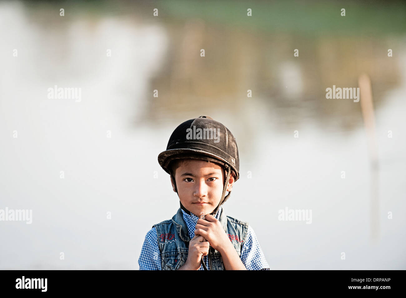 Jeune garçon asiatique porte un chapeau d'équitation prêt à monter sur son poney, debout regardant et souriant dans l'appareil photo Banque D'Images