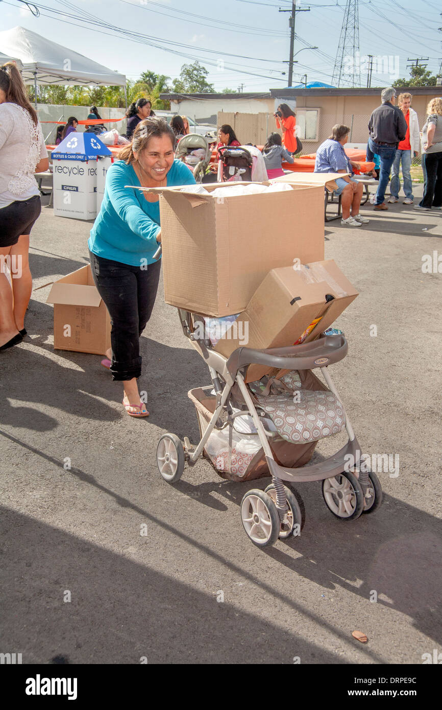 Une femme au foyer hispaniques utilise une poussette de bébé pour transporter de lourdes boîtes de dons en nourriture à partir d'un site de bienfaisance dans un taudis de Stanton, CA. Banque D'Images