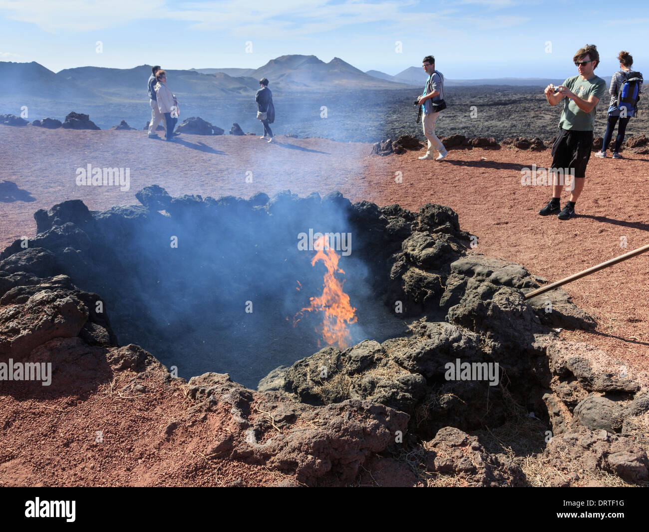 Les touristes regarder une démonstration de broussailles d'allumer avec la chaleur de l'évent volcanique sur la Montagne de feu dans le Parc National de Timanfaya, Lanzarote, Espagne Banque D'Images