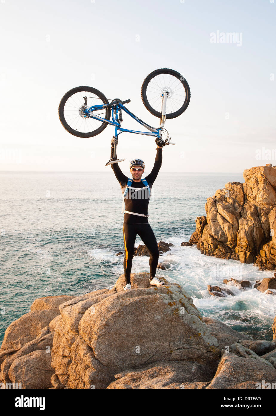 Man lifting son vtt avec un paysage marin en arrière-plan Banque D'Images