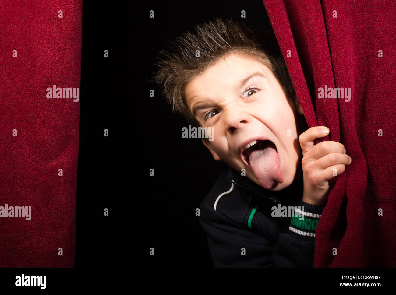 Enfant bâton dehors sa langue.apparaissant sous le rideau Banque D'Images