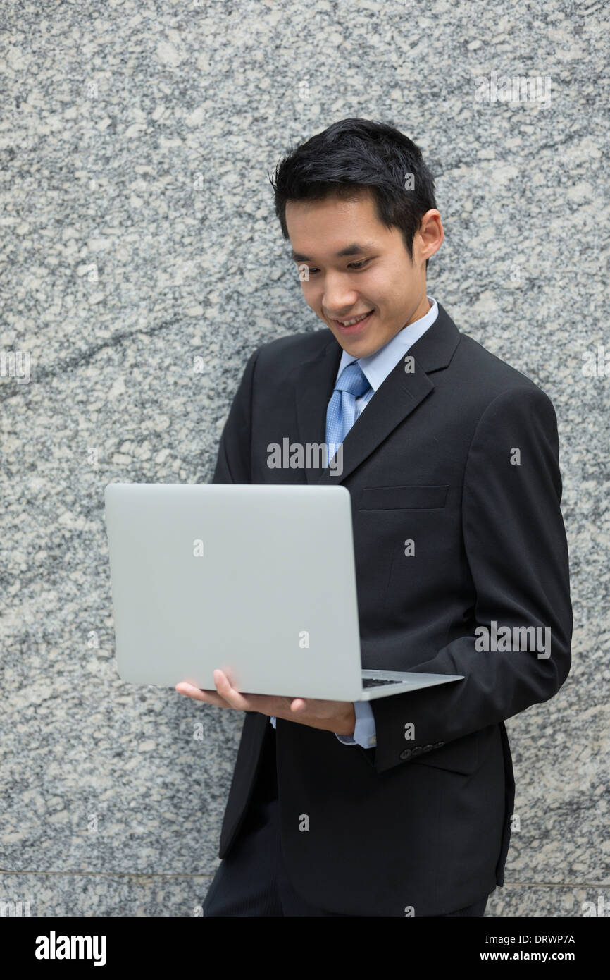 L'homme d'affaires chinois en utilisant son ordinateur portable des portes en ville moderne. Le concept d'affaires sur rendez-vous. Banque D'Images