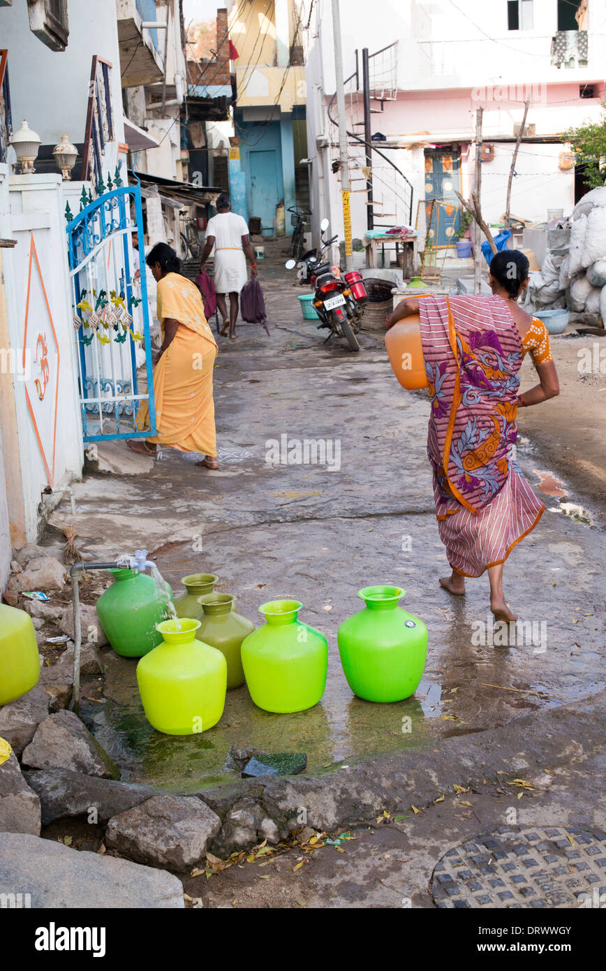 Les femmes indiennes le remplissage des pots en plastique avec de l'eau d'un tube de mesure dans une rue village. L'Andhra Pradesh, Inde Banque D'Images