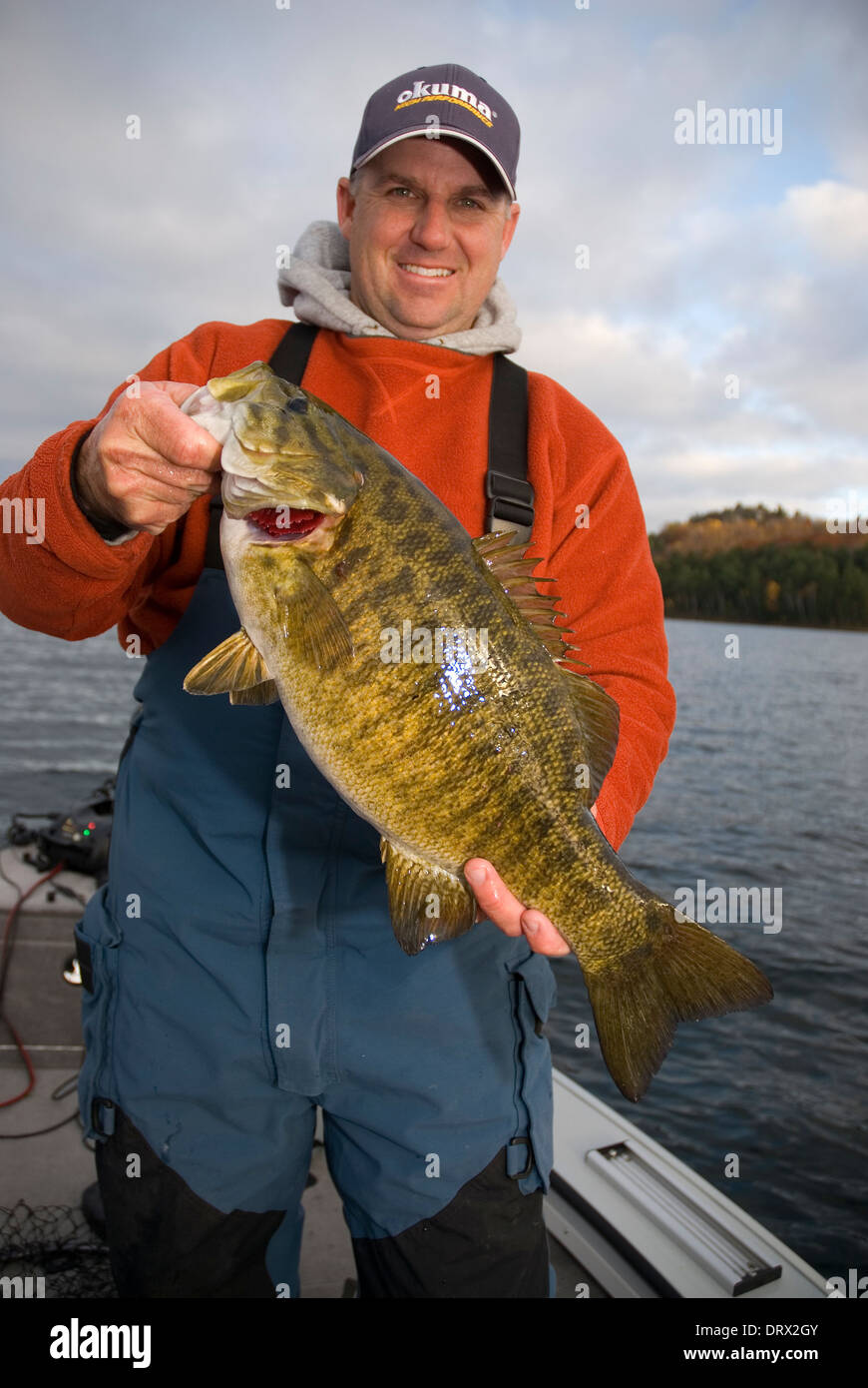 Fisherman holding up a l'achigan à petite bouche énorme de son bateau sur un lac dans le Nord de l'Ontario. Banque D'Images