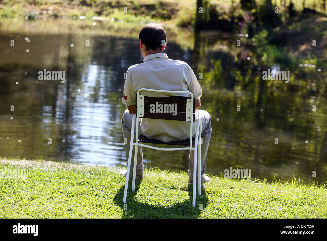 Un homme assis dans une chaise au bord de la rivière et appréciant le calme, vue arrière arrière bien-être Banque D'Images