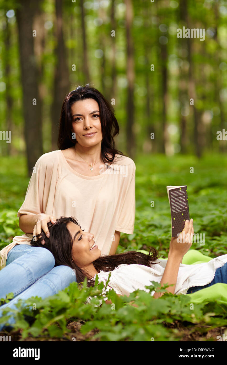 Fille avec la tête sur les genoux de sa mère la lecture d'un livre à un pique-nique dans une forêt Banque D'Images